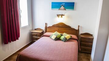 A bedroom with a wooden bed, two nightstands, a wall-mounted lamp, a window with curtains, and a painting of a pier.