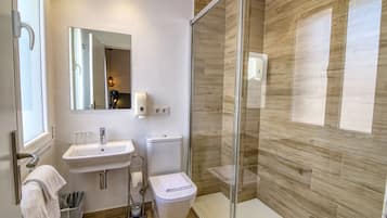 Un baño moderno con ducha de vidrio, lavamanos con espejo e inodoro.