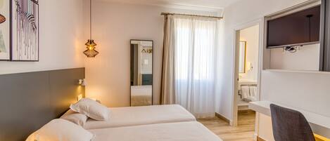 A hotel room with two beds, a desk, a chair, a TV, and a bathroom visible through an open door.