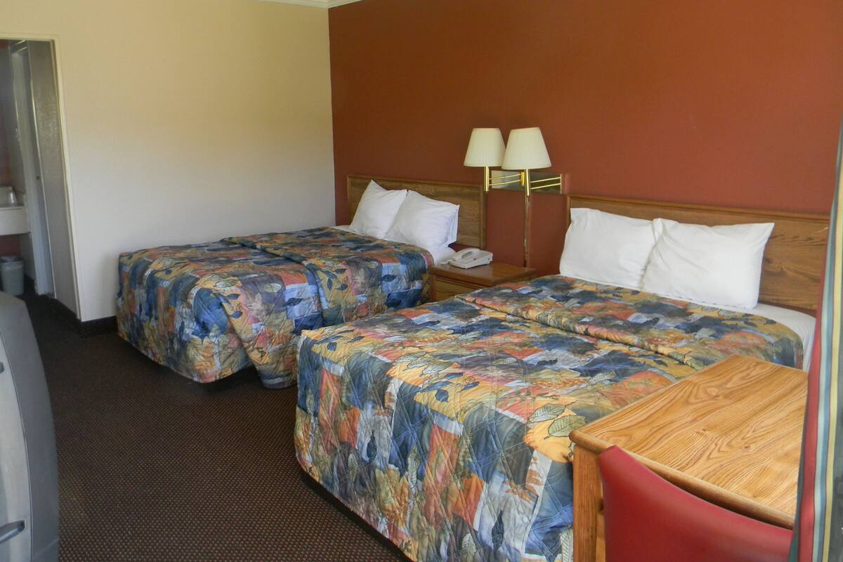 A hotel room with two beds, a wooden nightstand, a lamp, and a small table.