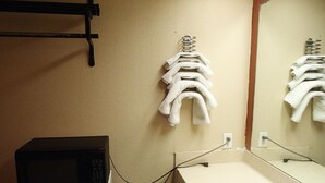 A bathroom with a white sink, a mirror, and a towel rack with towels. There is a microwave on a small white appliance, and a power outlet is visible on the wall. - Sunrise Inn (Lake Charles)