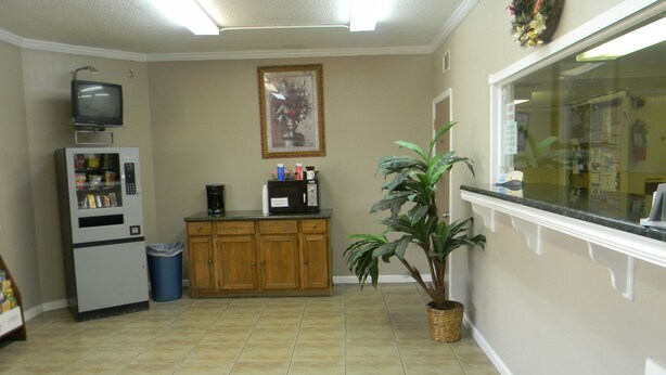 A kitchen with a microwave, a small refrigerator, a trash bin, wooden cabinets, and a potted plant. - Sunrise Inn (Lake Charles)