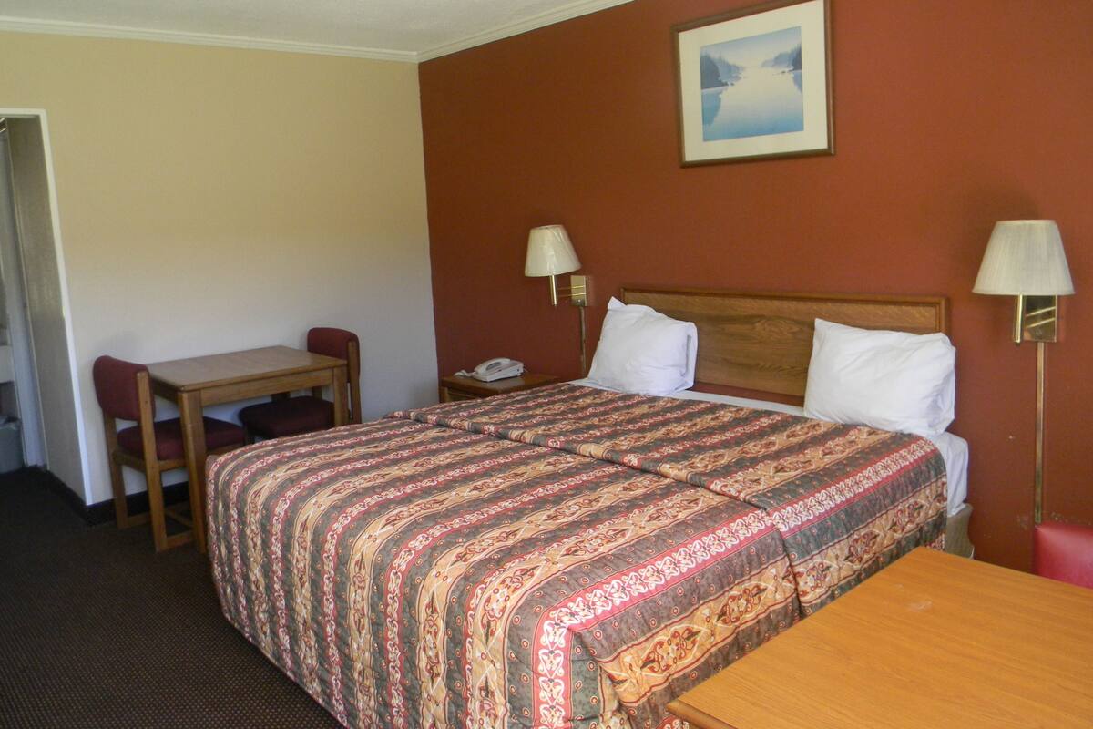 A hotel room with a bed, a desk, a chair, and two bedside lamps.