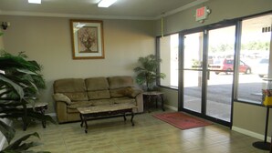 A lobby with a beige sofa, a coffee table, a small table, and a potted plant. - Sunrise Inn (Lake Charles)