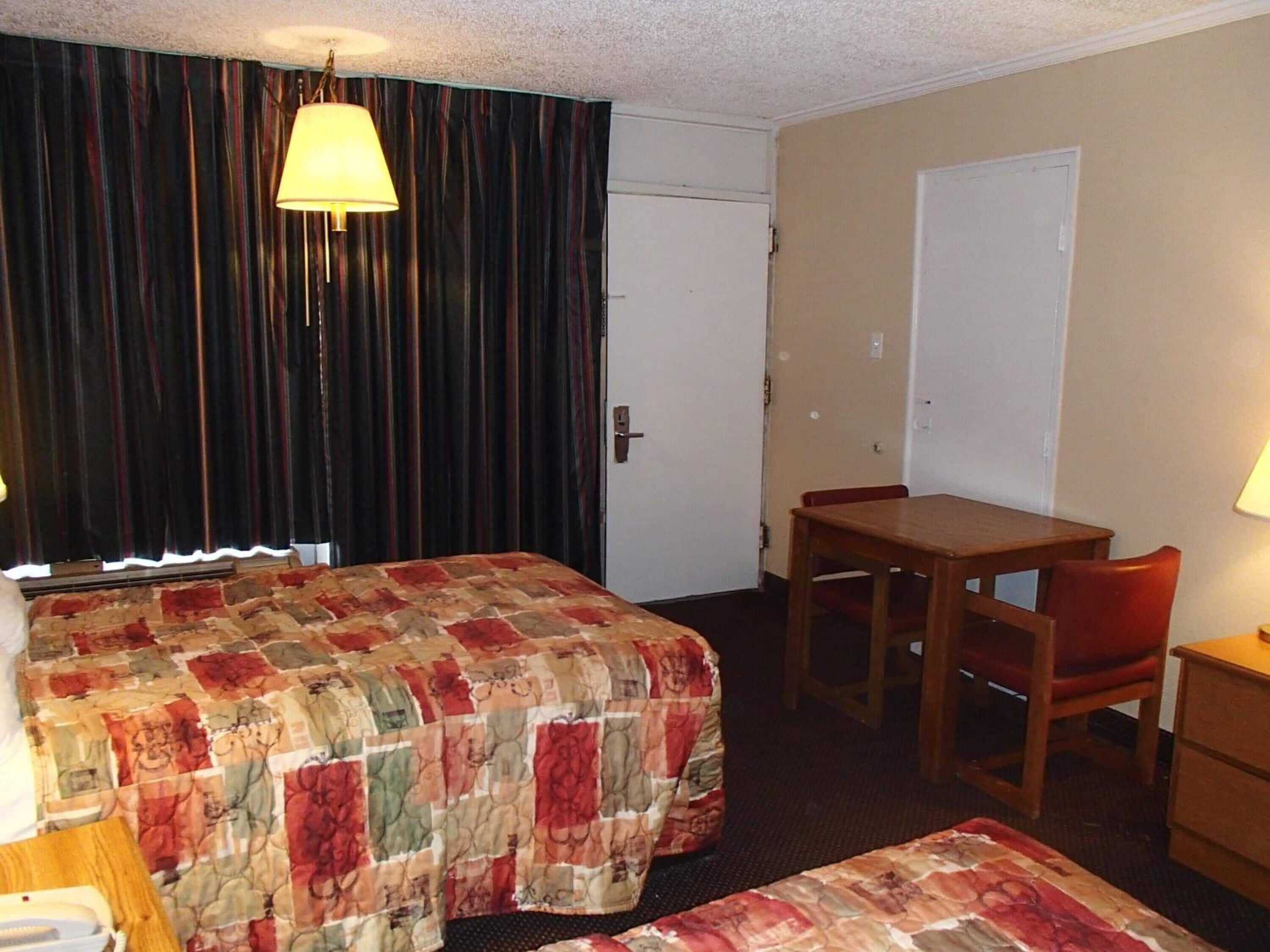 A hotel room with a bed, a desk, a chair, and a lamp.