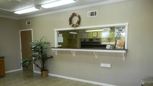 A reception area with a reception desk, a clock, a sign indicating pool hours, and a plant. - Sunrise Inn (Lake Charles)