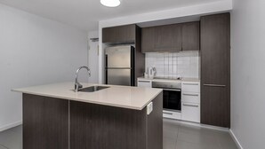 Une cuisine moderne avec des meubles de rangement en bois foncé, un réfrigérateur en acier inoxydable, un four encastré et un plan de travail de couleur claire doté d’un évier.