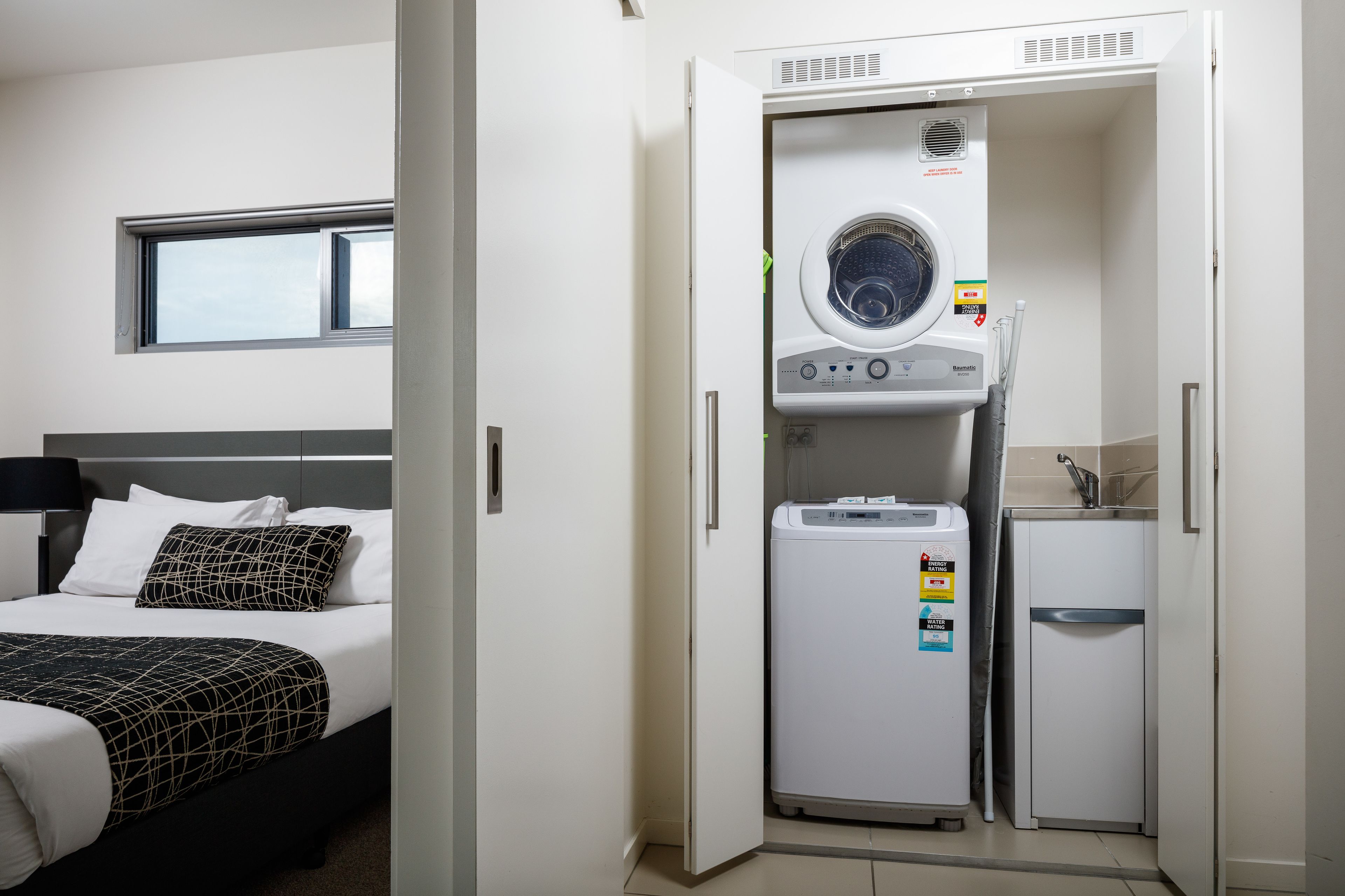 A hotel room with a bed, a washing machine, and a small kitchenette.