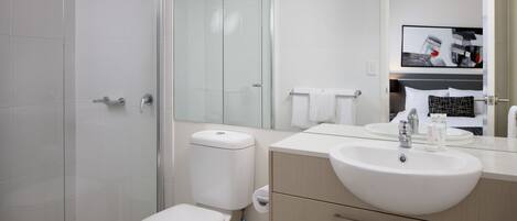 Ein modernes Badezimmer mit Duschkabine aus Glas, Toilette in Weiß, Waschbecken mit Spiegel und Deckenventilator.