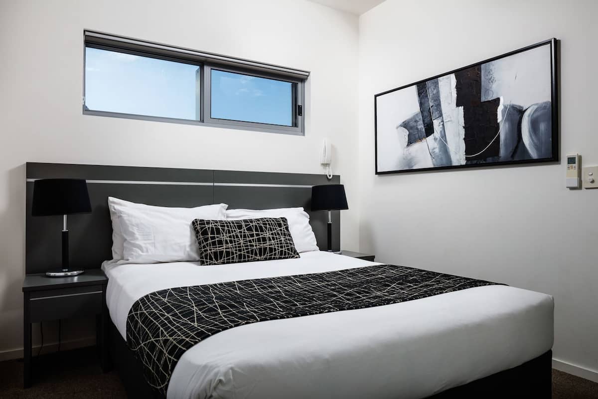 Une chambre d’hôtel avec un lit, deux tables de chevet, une fenêtre et un tableau au mur.