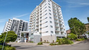 Un immeuble moderne à plusieurs étages, doté de balcons, d’une entrée bien visible et surplombant un ciel dégagé.