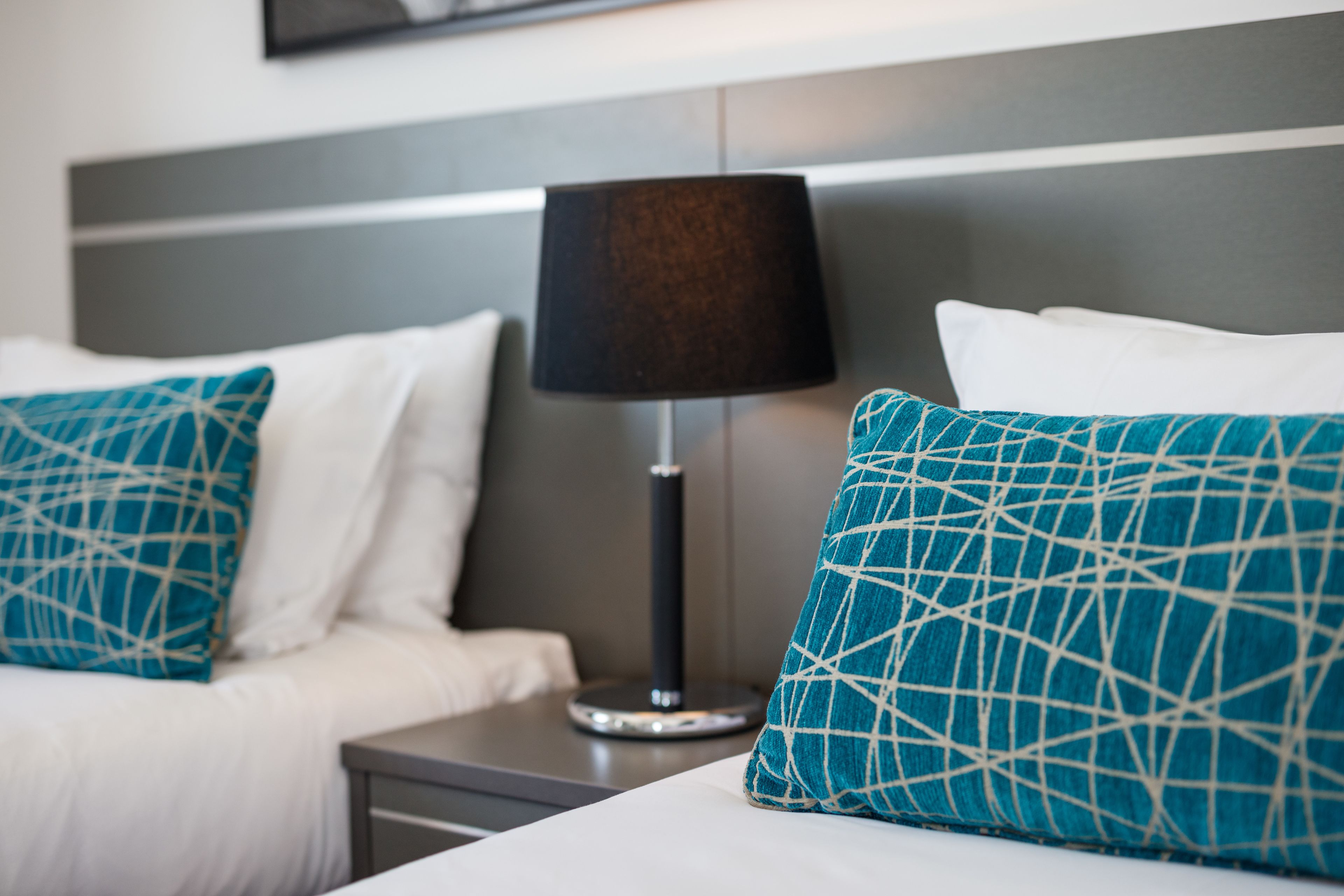 Una habitación de hotel con una cama, una mesita de noche, una lámpara y un cabecero.