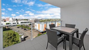 Un balcon avec une table et des chaises, donnant sur un parking et des immeubles.