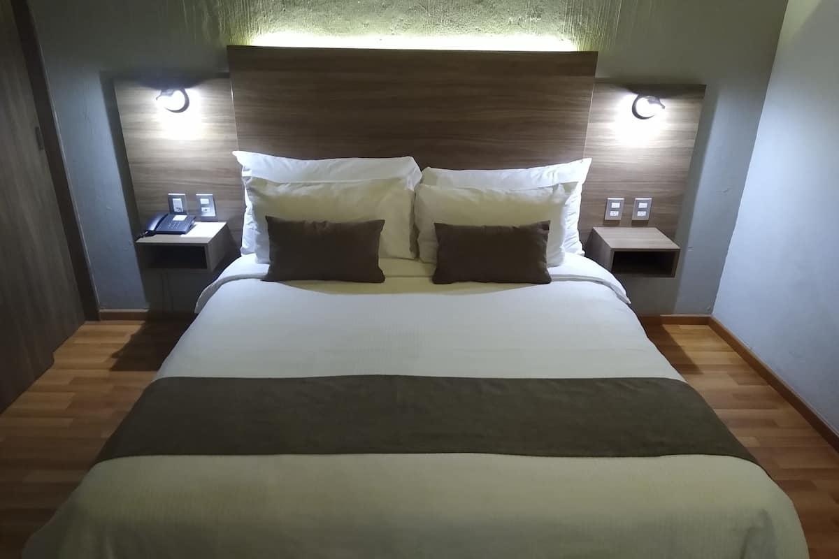 A modern hotel room with a large bed, bedside tables, and a headboard with integrated lighting.