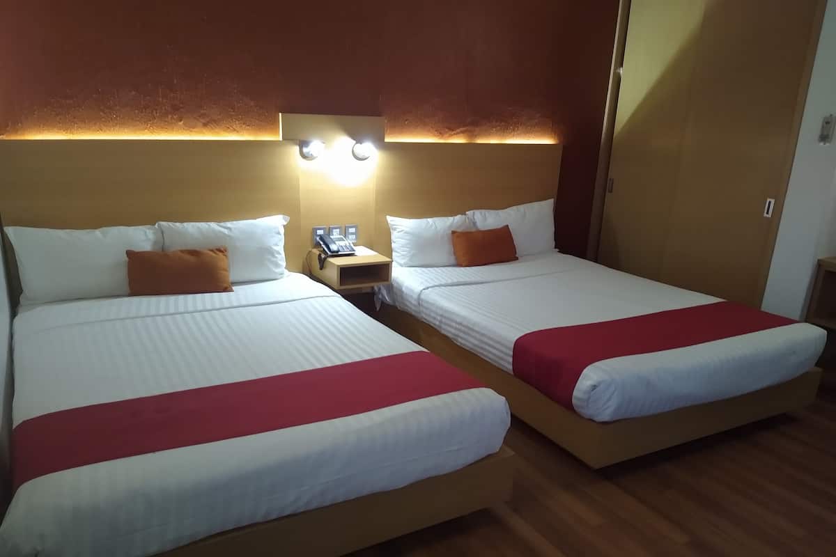 A hotel room with two beds, each with white bedding and red accents, a nightstand with a phone, and wall-mounted lighting.
