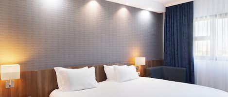 A hotel room with a large bed, two bedside lamps, a telephone, and a window with curtains.