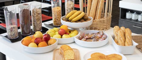 A buffet table with various food items including fruits, bread, and pastries.