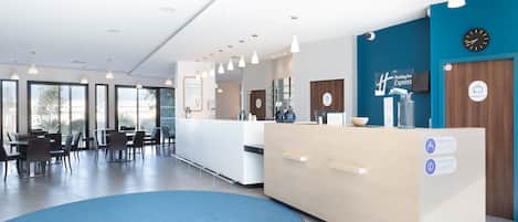 A hotel reception area with a large blue carpet, a reception desk, and a clock on the wall.
