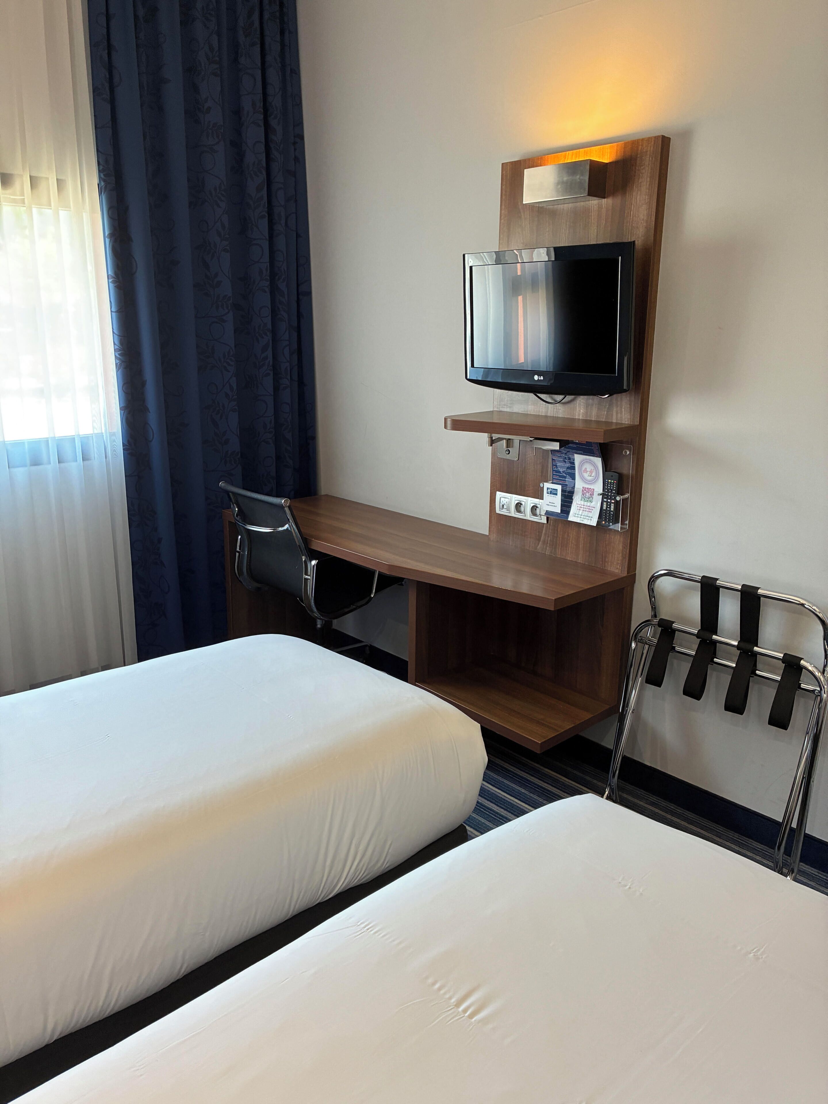 Ett hotellrum med två sängar, ett skrivbord med en tv, en stol och en klädställning.