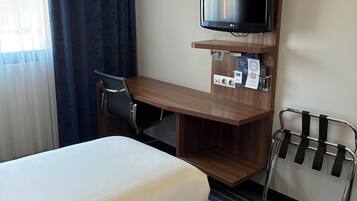 Ett hotellrum med två sängar, ett skrivbord med en tv, en stol och en klädställning.