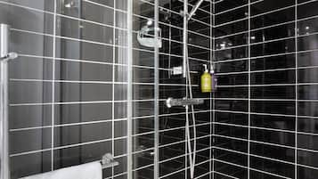 Un baño con cabina de ducha de vidrio, una toalla blanca colgada en un perchero y una botella de champú en la pared.