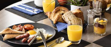 Ein Frühstückstisch mit Croissants, Toast, Würstchen, Eiern und Orangensaft.