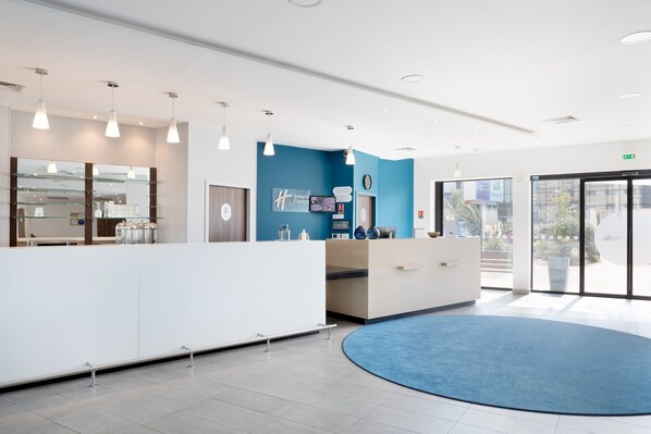 A modern reception area with a blue accent wall, a reception desk, and a glass display case. - Holiday Inn Express Marseille Airport by IHG (Vitrolles)