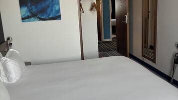 Een hotelkamer met een groot bed, een schilderij aan de muur, een deur naar een andere kamer en een spiegel.