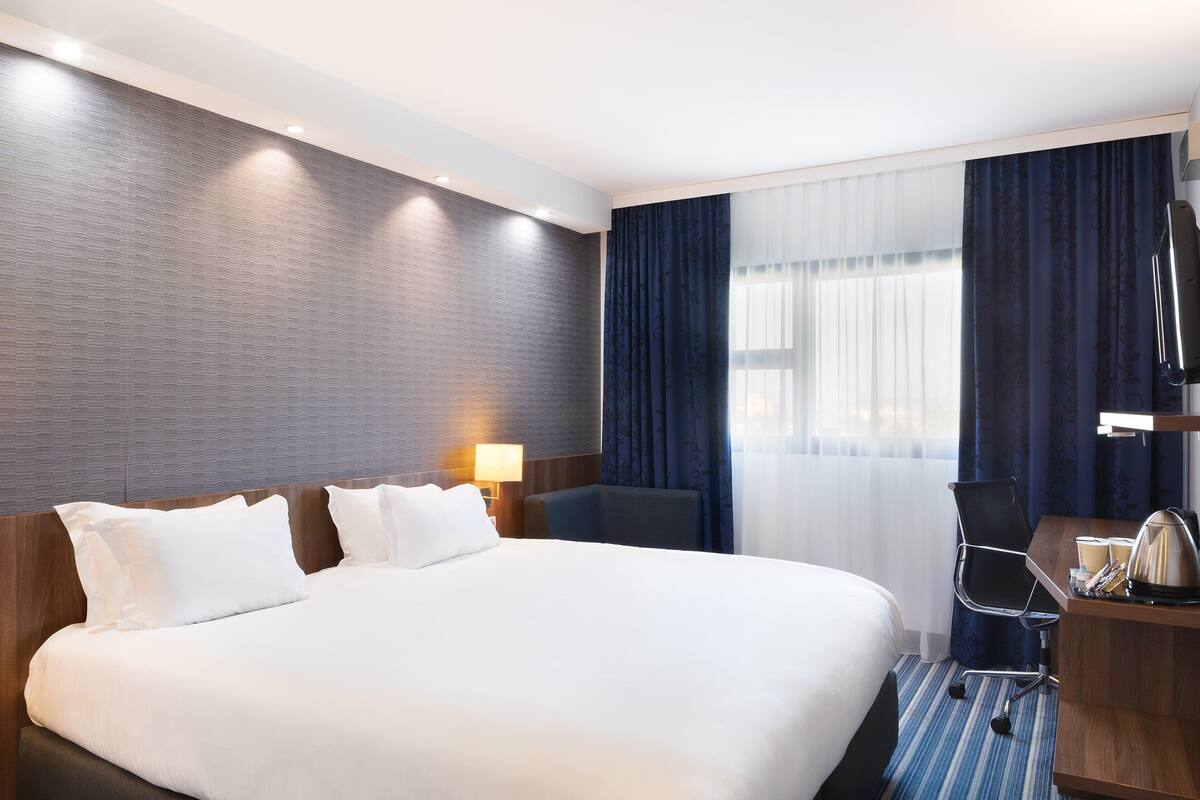 A hotel room with a large bed, a desk, a chair, a lamp, and a television.