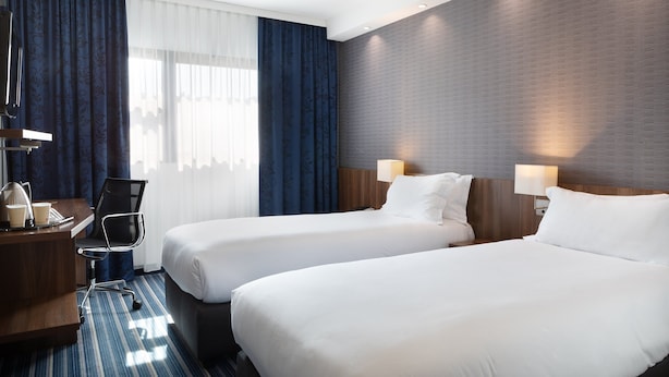 Une chambre d’hôtel avec deux lits, un bureau avec une chaise, une lampe de bureau et un téléphone.