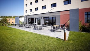 Un bâtiment moderne doté d’un toit plat, de grandes fenêtres et d’un patio aménagé avec des sièges extérieurs.