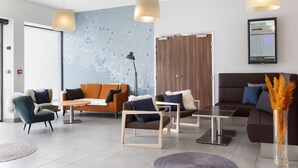 Un hall d’hôtel moderne, doté d’espaces aménagés avec des sièges, d’une carte affichée au mur et d’une présentation encadrée.