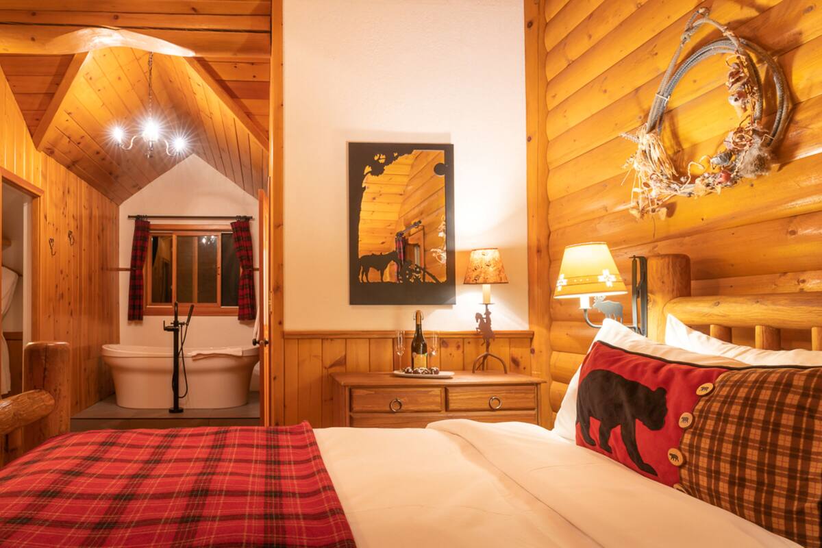Une chambre dans un chalet en bois, comprenant un lit, une commode en bois, une salle de bain avec baignoire et un miroir fixé au mur.