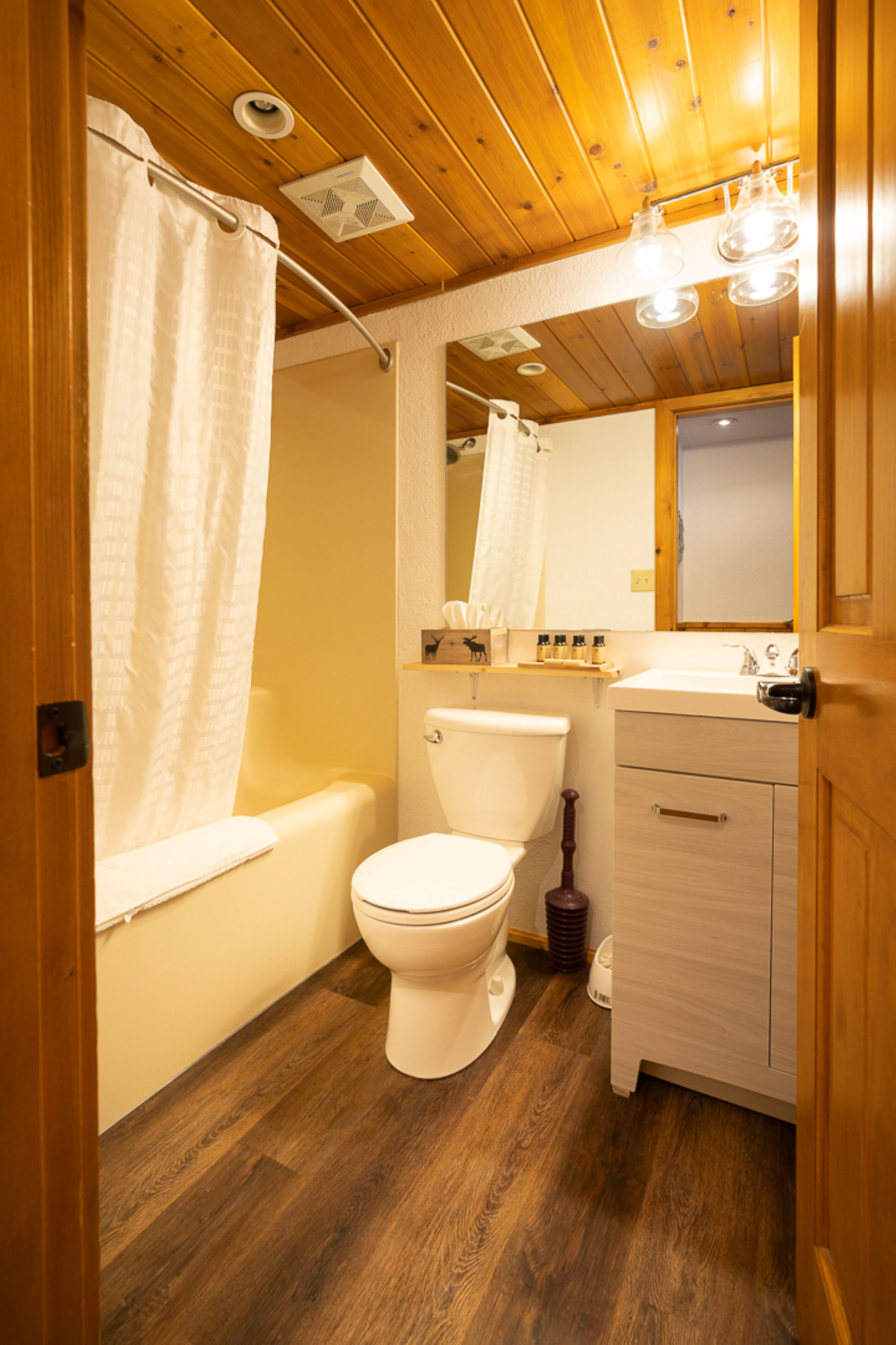A bathroom with a wooden floor, a white toilet, a bathtub, and a sink with a mirror above it.