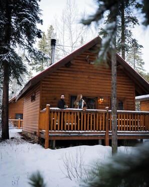 Una cabaña de madera con porche, rodeada de árboles cubiertos de nieve.
