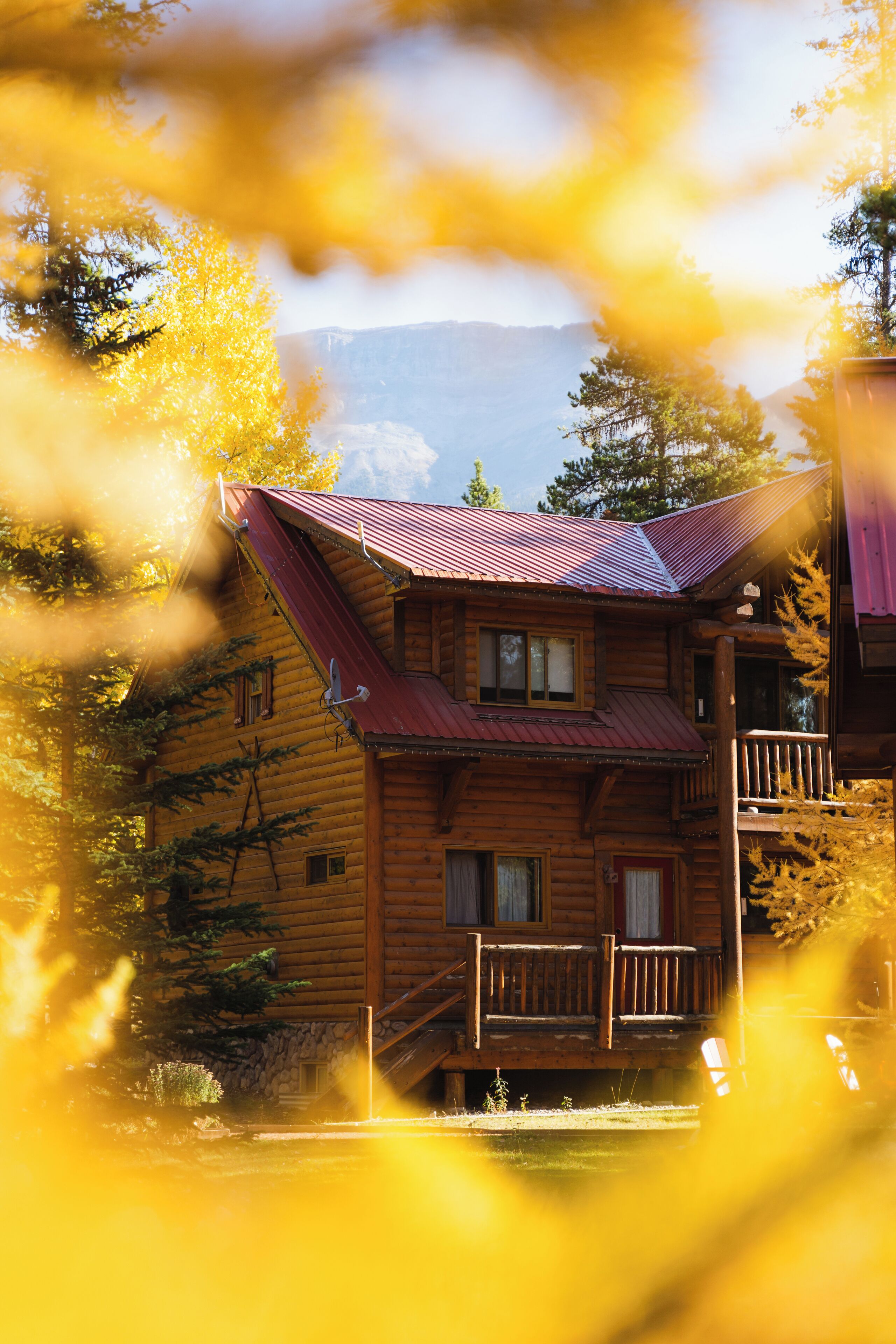 A wooden cabin with a red roof, a balcony, and a mountain backdrop.