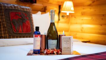 A bed with a red moose patch, a bottle of wine, a massage oil bottle, and a candle on a plaid blanket.