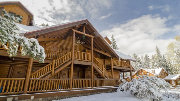 Una cabaña de madera con cimientos de piedra, barandillas de madera y un paisaje cubierto de nieve.
