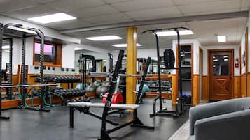 Een sportschool met diverse fitnessapparaten, waaronder krachttoestellen, banken en losse gewichten.