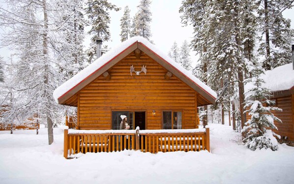 Una cabaña de madera con techo nevado y un porche de madera.