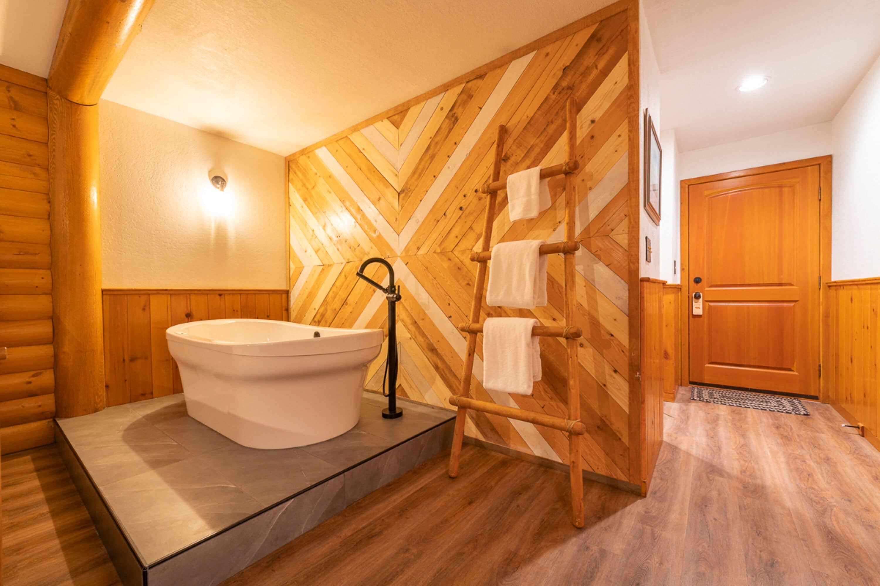 A wooden interior with a freestanding bathtub, a wooden towel rack, and a wooden door.