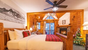 A log cabin bedroom with a bed, a fireplace, a Christmas tree, and a mountain painting on the wall.