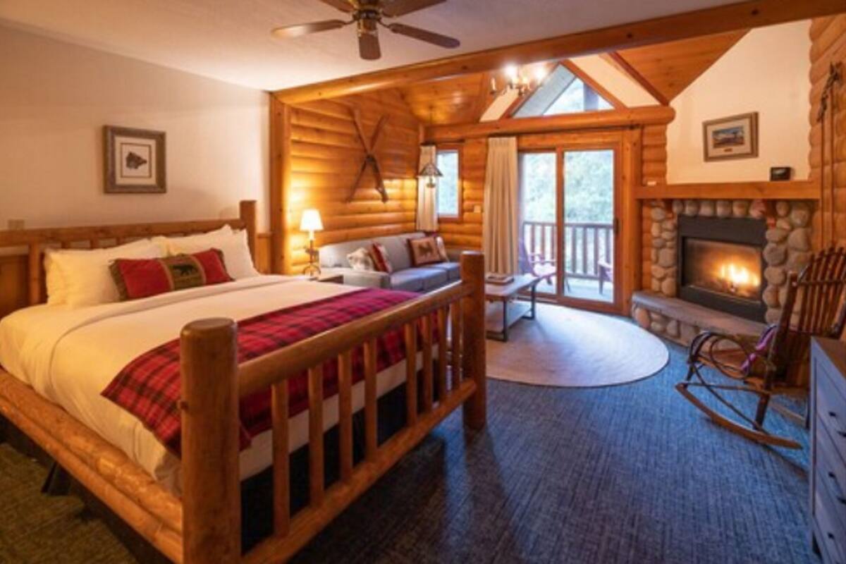 Une chambre dans un chalet en rondins, avec un lit, un fauteuil à bascule, une cheminée et un balcon.