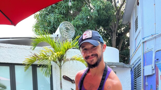 Une personne tenant un plateau de nourriture grillée près d’une piscine, avec un mur blanc et des plantes en pot en arrière-plan.