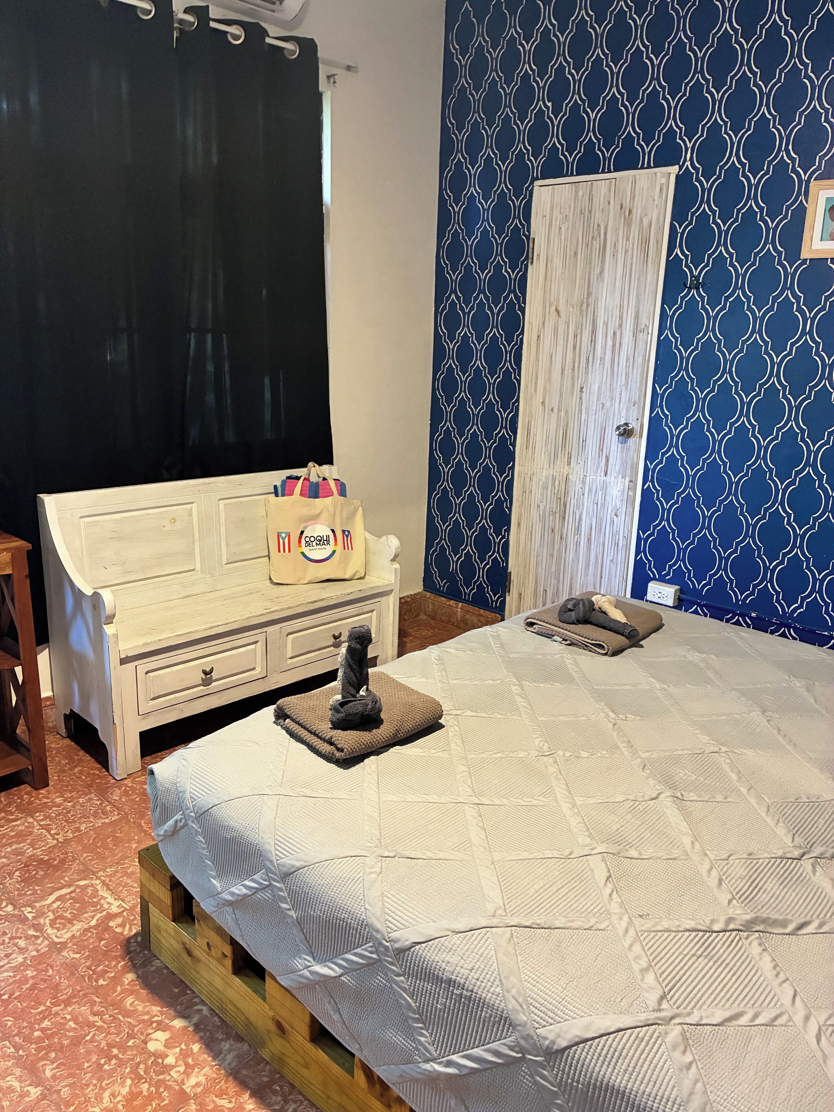 A bedroom with a bed, a wooden nightstand, a wardrobe, and a patterned wall.