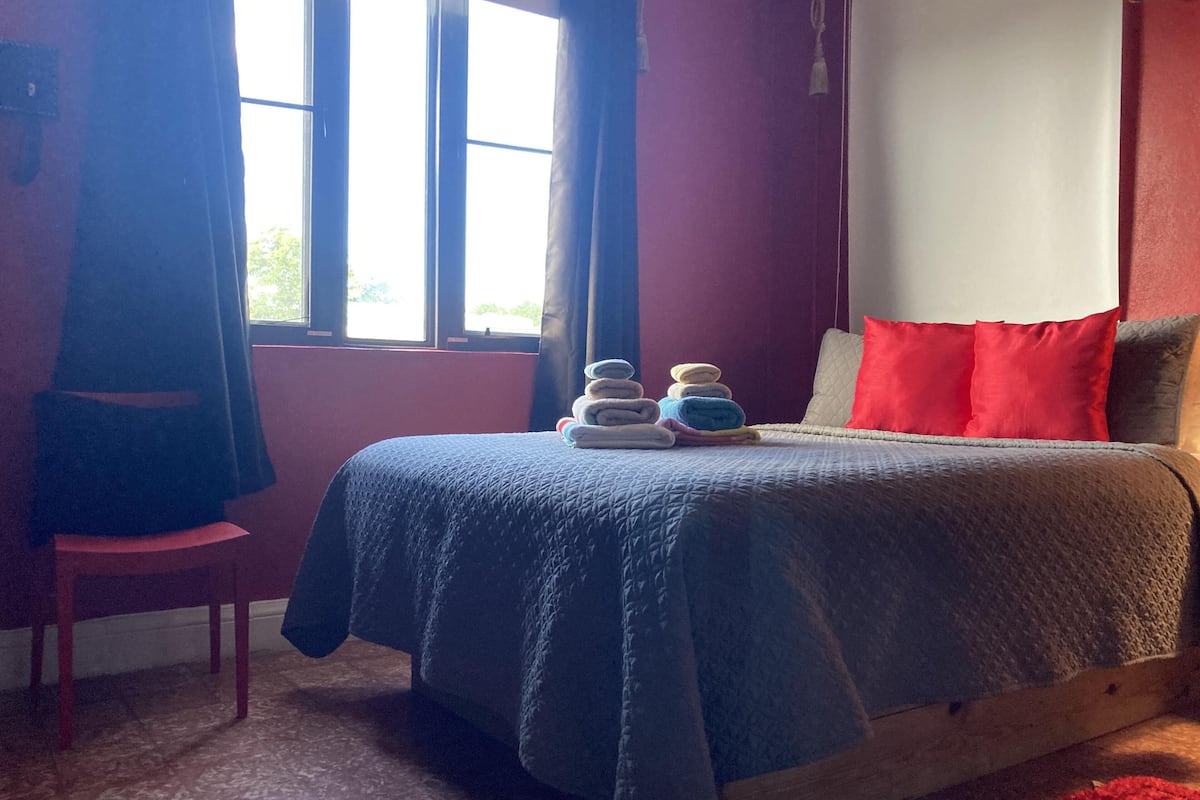 A bedroom with a bed, a chair, a window, and a view of greenery outside.