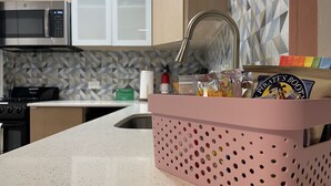 Une cuisine équipée d’un four à micro-ondes, d’un évier et d’un panier rose contenant divers objets.