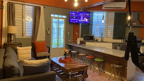 Un salon comprenant un canapé, une table basse et un téléviseur. Il y a également un coin cuisine avec un four à micro-ondes et un évier.