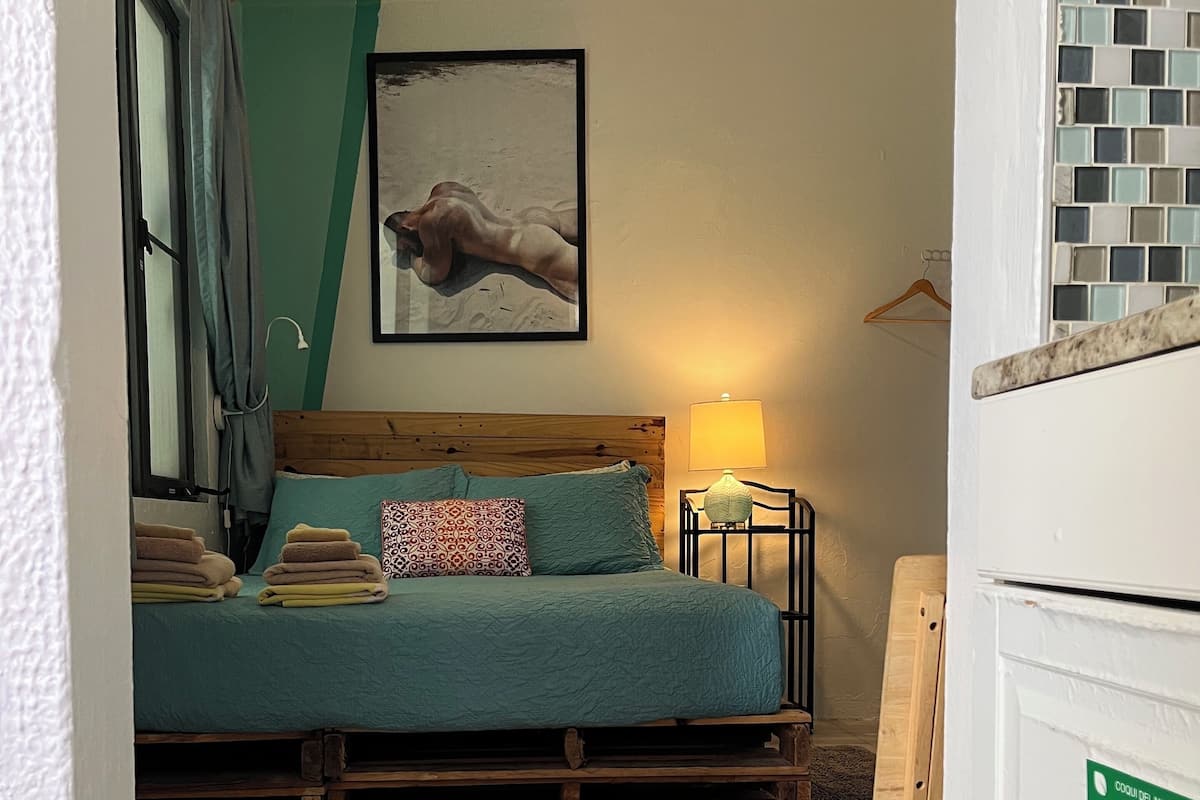 A bedroom with a bed, pillows, a bedside lamp, a framed picture on the wall, and a sign on the door.