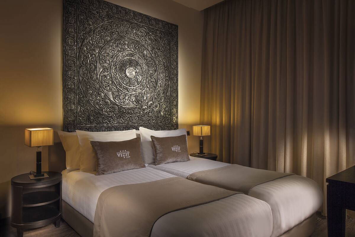 A double bed with two pillows, a nightstand with a lamp, and a large tapestry on the wall.